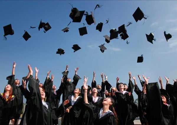 Group of graduates celebrating by throwing caps in the air during a sunny day.
